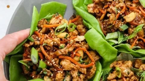 Plate of Thai chicken lettuce wraps garnished with herbs and spices.